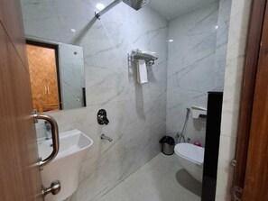 A bathroom with a marble wall, a sink, a toilet, and a shower area. - Hotel Arg (Araria)