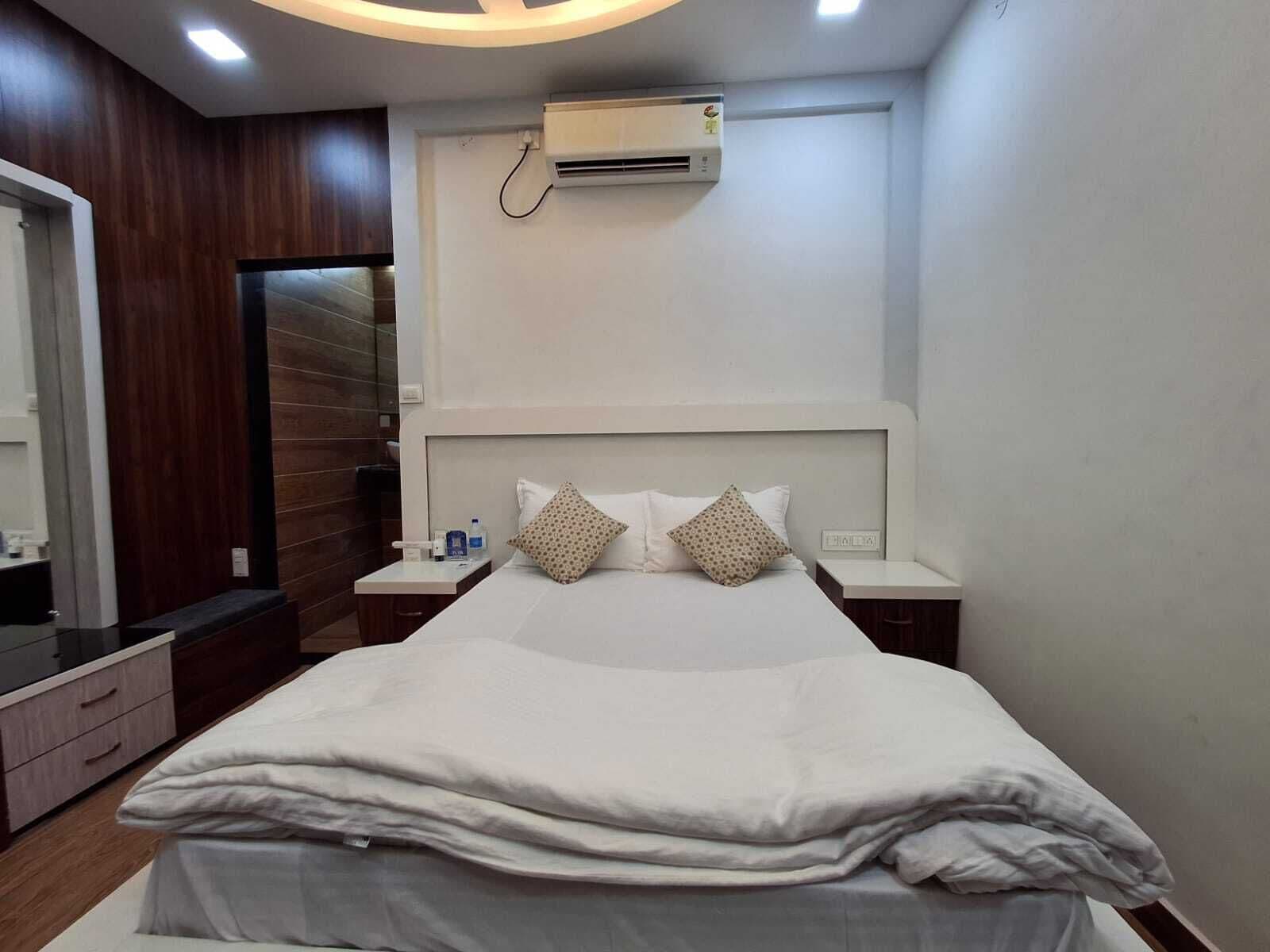 Une chambre d’hôtel moderne dotée d’un grand lit, de deux tables de chevet, d’un appareil de climatisation et d’un mur décoratif en bois.