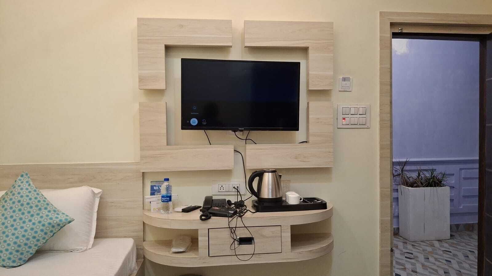 Une chambre d’hôtel équipée d’une télévision fixée au mur, d’un petit bureau avec une bouilloire, d’une bouteille d’eau et d’un téléphone.