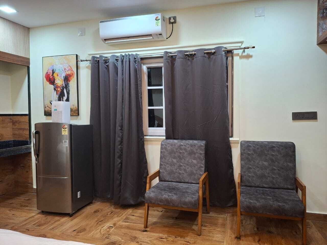 A compact kitchen with a refrigerator, two chairs, and a window with curtains.
