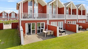 A two-story building with a balcony, large windows, and a patio area with outdoor seating. - 5 Star Holiday Home in Lokken (Lokken)