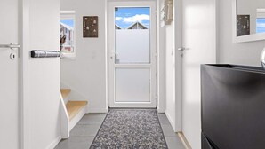 A hallway with a white door leading to a balcony, a small rug, and a refrigerator. - 5 Star Holiday Home in Lokken (Lokken)