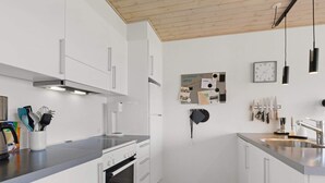 A modern kitchen with white cabinetry, a stainless steel countertop, a built-in oven, and a wall-mounted clock. - 5 Star Holiday Home in Lokken (Lokken)