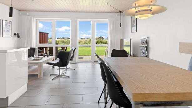 A modern kitchen with a wooden ceiling, large windows, and a dining area with a long table and chairs. - 5 Star Holiday Home in Lokken (Lokken)