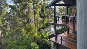 A multi-level wooden deck with outdoor seating, surrounded by dense forest and overlooking a body of water. - Cosy Mountain house w/fire and pool on Tamborine Mountain! (Tamborine Mountain)