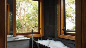A bathroom with a black bathtub, a wooden window frame, and a view of trees outside. - Cosy Mountain house w/fire and pool on Tamborine Mountain! (Tamborine Mountain)
