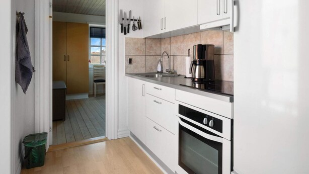 A modern kitchen with white cabinets, a stainless steel coffee maker, and an oven. - 5 Star Holiday Home in Lokken (Lokken)