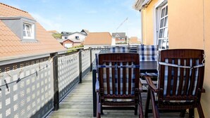 A wooden deck with two wooden chairs and a table, overlooking a residential area with houses and a clear sky. - 5 Star Holiday Home in Lokken (Lokken)