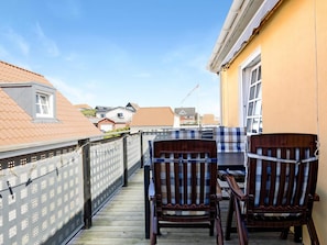 Une terrasse en bois avec deux chaises et une table, d’où l’on a vue sur un quartier résidentiel avec ses maisons et un ciel dégagé.