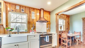 Una cocina con armarios de madera, una campana extractora de acero inoxidable, un lavamanos y una mesa de comedor con sillas.