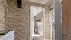 Une pièce avec un mur en pierre, un plancher en bois, une armoire blanche avec des tiroirs et une porte donnant sur une autre pièce.
