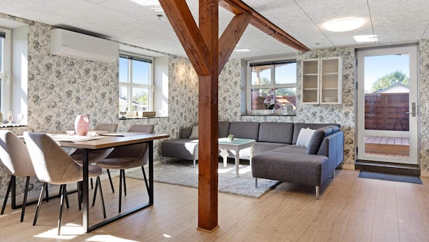 Un vaste espace de vie doté d’une structure en poutres apparentes, une table à manger avec des chaises, un canapé et une petite table basse.