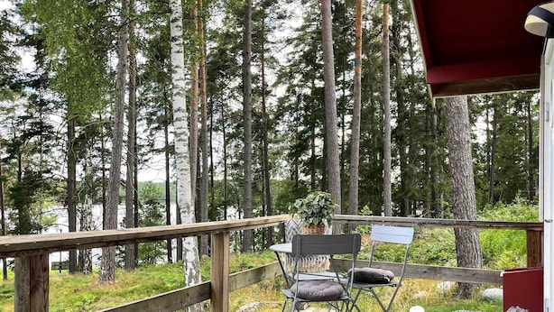 A wooden deck with two chairs and a table, overlooking a forest and a body of water. - 5 Star Holiday Home in Vaxholm (Vaxholm)