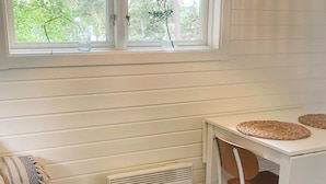 A room with a white table, two woven placemats, a chair, a radiator, and a window with a view of trees. - 5 Star Holiday Home in Vaxholm (Vaxholm)