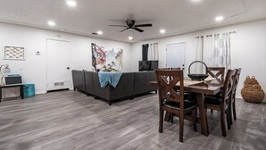 Ein modernes Wohnzimmer mit einer Couch, einem Esstisch, Stühlen, einem Deckenventilator und Kunstwerken an den Wänden.