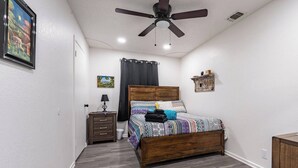 Ein Schlafzimmer mit einem hölzernen Bett, einem Nachttisch, einem Deckenventilator und einem kleinen Regal.