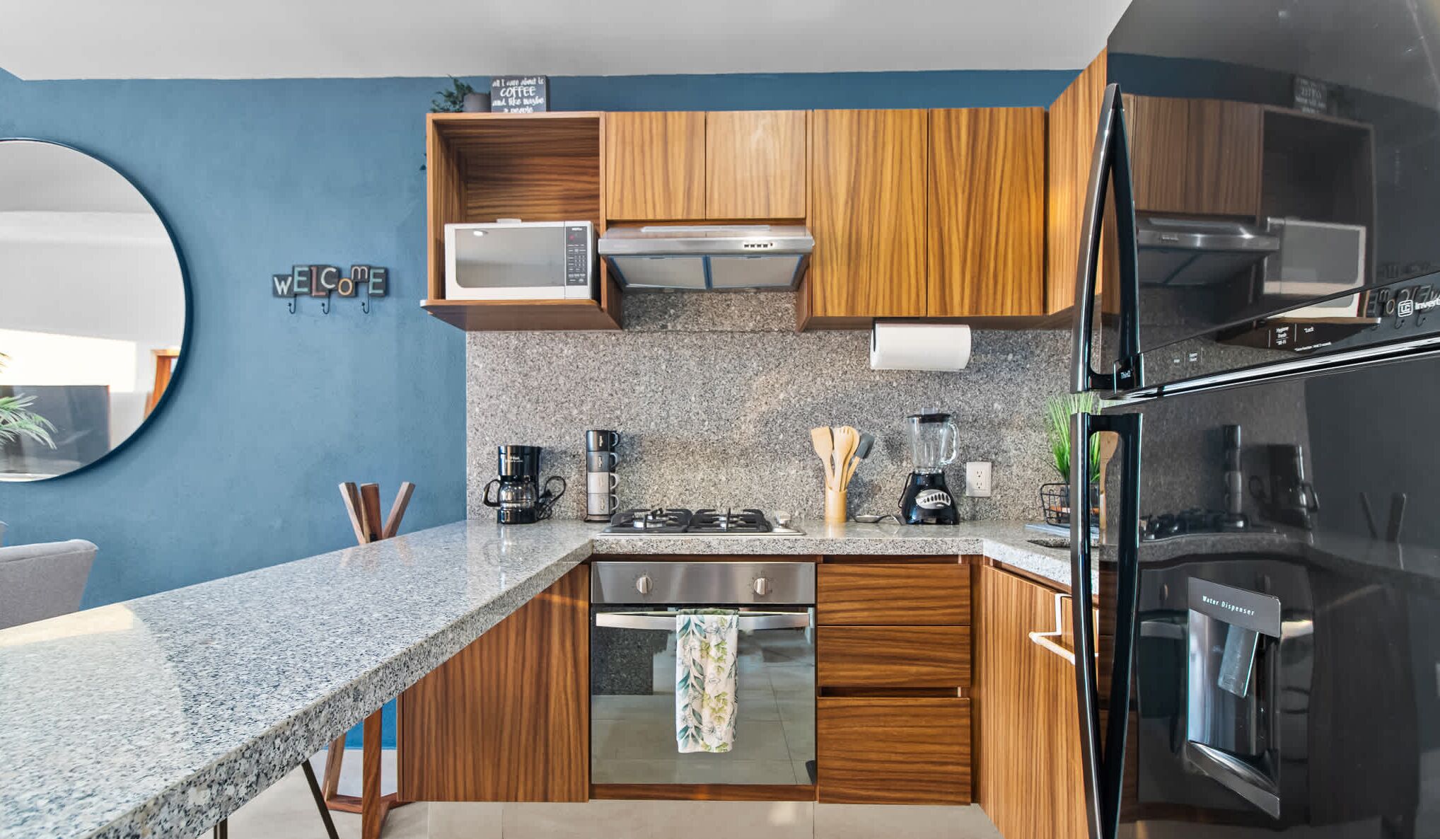 Una cocina moderna con encimeras de granito, armarios de madera y electrodomésticos de acero inoxidable, incluyendo un horno empotrado.