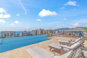 A rooftop pool area with lounge chairs and a view of the ocean and buildings.