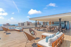 Terraço no telhado com áreas de estar, espaço coberto para refeições e vista para o horizonte da cidade.