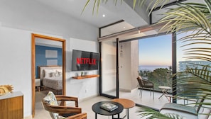 Een moderne woonkamer met een grote televisie waarop 'NETFLIX' wordt weergegeven, een balkon met uitzicht en een gezellige zithoek.