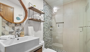Een moderne badkamer met een groot wastafelmeubel, toilet, douche en een douchecabine met glazen wanden.