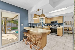 A modern kitchen with a large island, bar stools, wooden cabinets, and a view of the backyard.