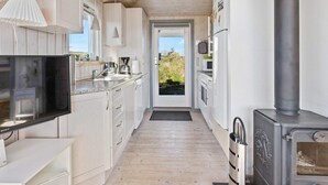 A narrow kitchen with wooden cabinets, a stove, and a television. - 5 Star Holiday Home in Lokken (Lokken)