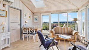 A cozy room with wooden walls, a dining area with white chairs, a striped sofa, and a table. - 5 Star Holiday Home in Lokken (Lokken)