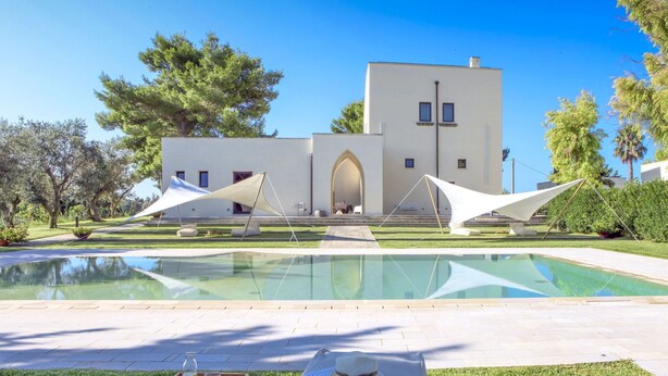 Ein modernes Gebäude mit Pool, Sitzgelegenheiten im Freien und blauem Himmel.