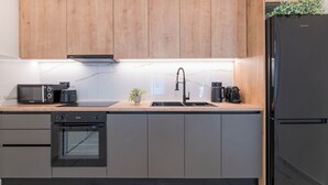 A modern kitchen with wooden cabinets, a built-in oven, a sink, and a black refrigerator. - Adorable 2BR Apartment in Neos Kosmos (Athina)
