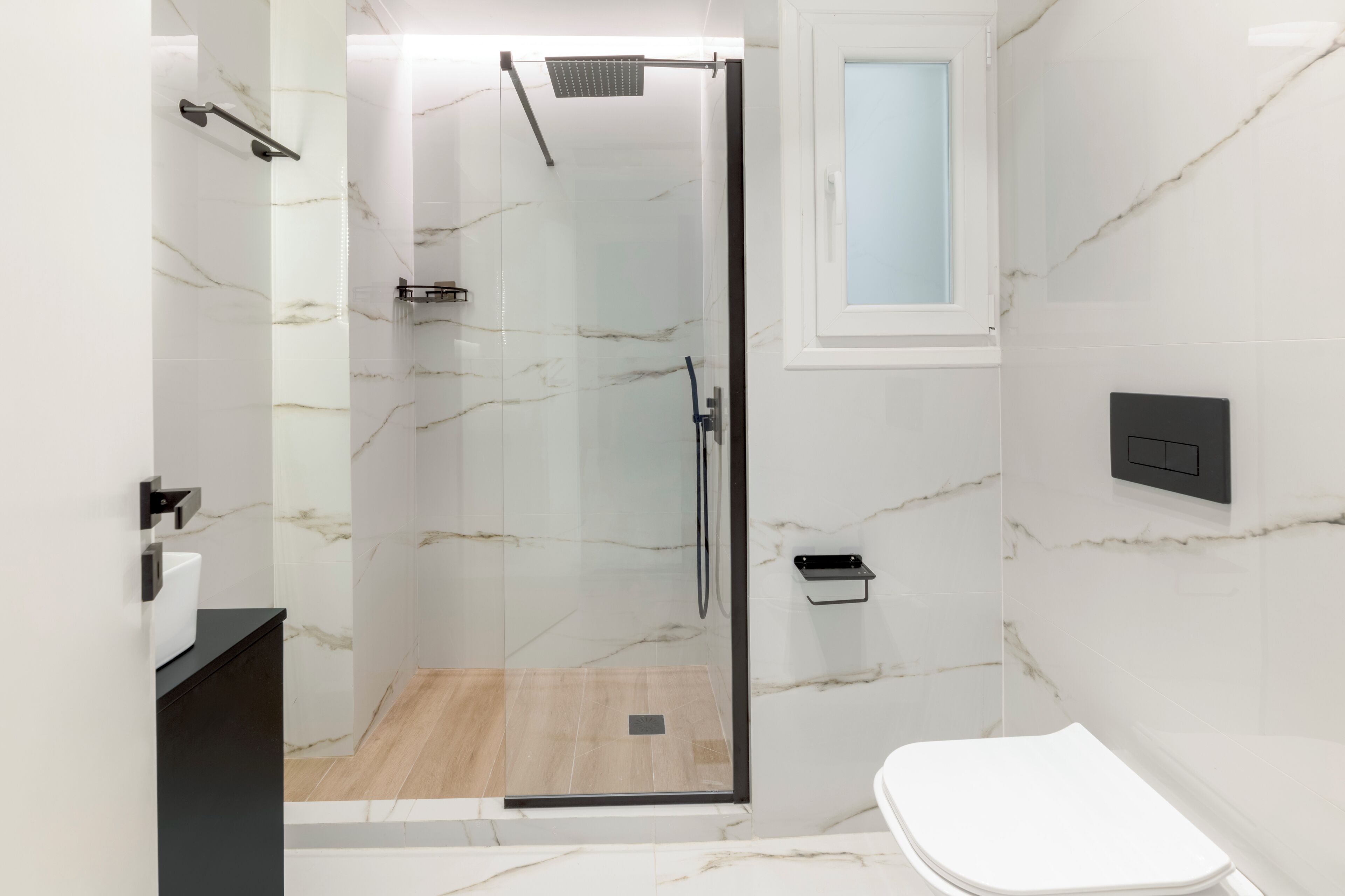 A modern bathroom with a glass-enclosed shower, a white toilet, and a black sink.