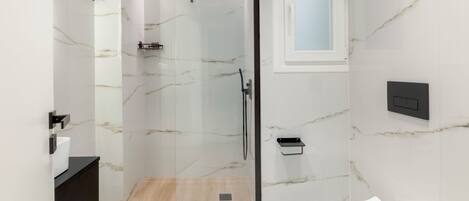 A modern bathroom with a glass-enclosed shower, a white toilet, and a black sink.