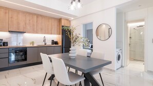 A modern kitchen with wooden cabinets, a built-in oven, and a dining area with a table and chairs. - Adorable 2BR Apartment in Neos Kosmos (Athina)