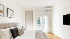A modern hotel room with a large bed, a flat-screen TV, and a view of the outdoors through a sliding glass door. - Adorable 2BR Apartment in Neos Kosmos (Athina)