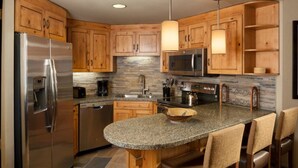A modern kitchen with wooden cabinets, stainless steel appliances, granite countertops, and a central island with bar stools.