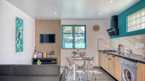 Ett modernt kök med en inbyggd tvättmaskin, en matplats med bord och stolar, en tv som är monterad på väggen och ett fönster med utsikt över grönområden.