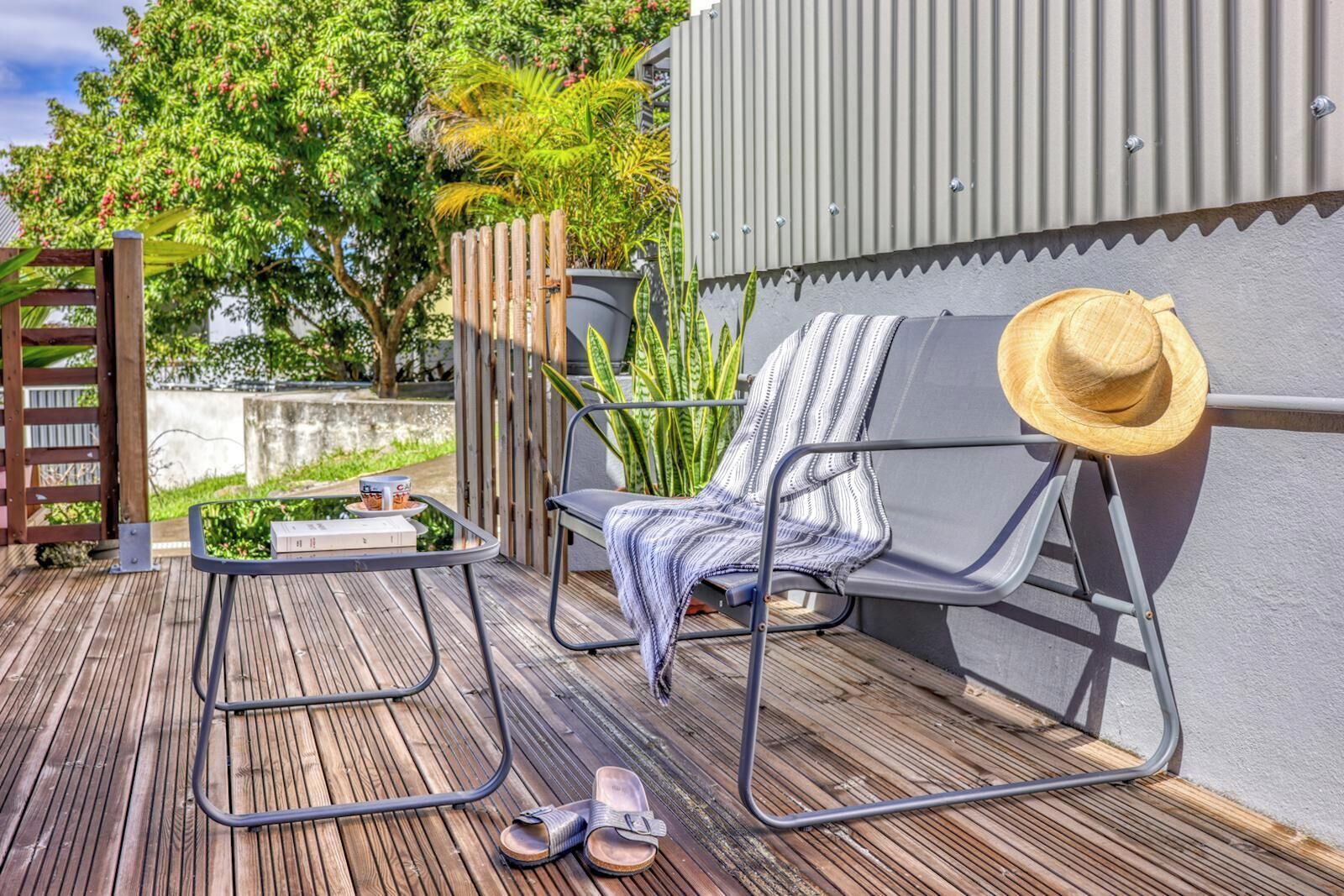 A wooden deck with a metal chair, a table with a drink, and a hat.