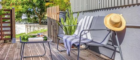 A wooden deck with a metal chair, a table with a drink, and a hat.