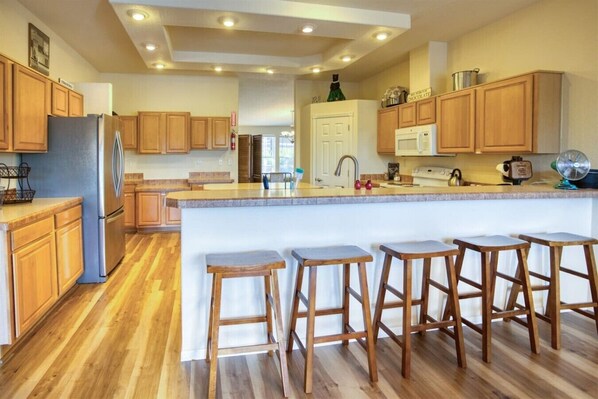 Una cocina moderna con armarios de madera, un refrigerador de acero inoxidable, una isla central con taburetes y un microondas.