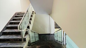 Una escalera con escalones de mármol y barandillas de vidrio, que conduce a un rellano con pared blanca y una puerta.