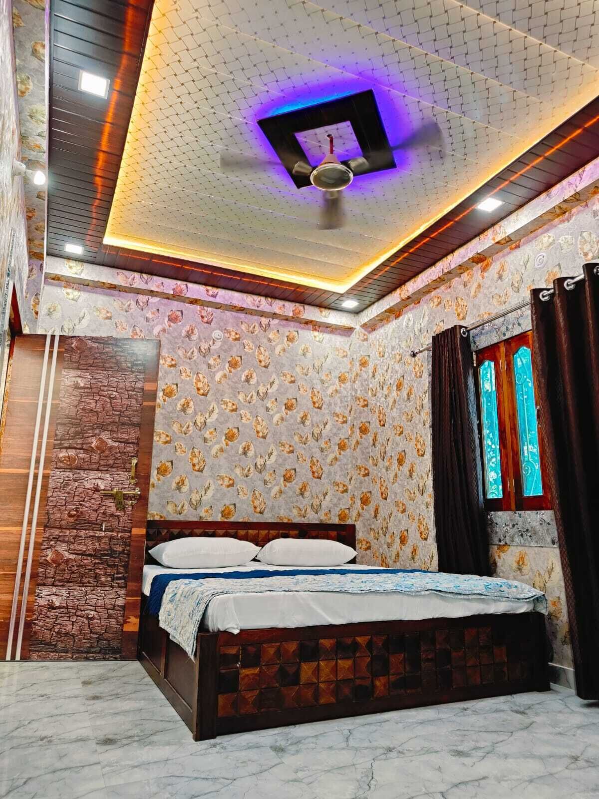 A bedroom with a bed, patterned wallpaper, a stone accent wall, a ceiling with a geometric light fixture, and a window with curtains.