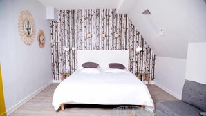Une chambre à coucher avec un lit, deux miroirs muraux, un papier peint à motifs, un canapé gris et une petite table en verre.