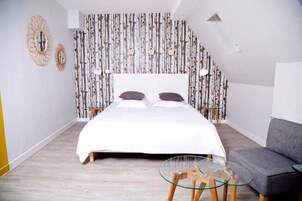 Quarto com cama, dois espelhos na parede, papel de parede estampado, sofá cinza e uma pequena mesa de vidro.