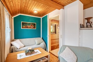 A cozy room with a wooden ceiling, teal walls, a sofa, a table with candles, and a door leading to another room.