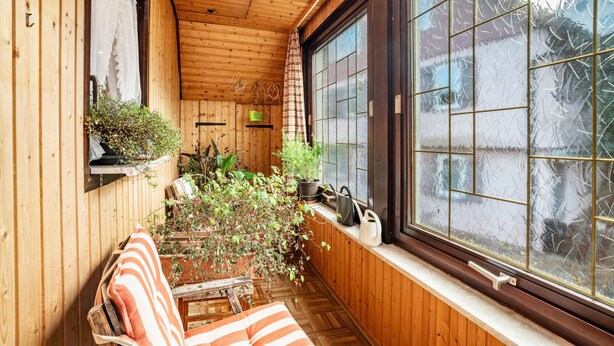 Une pièce en bois avec une grande fenêtre, un banc et des plantes en pot.