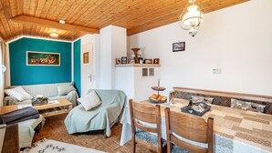 Une pièce chaleureuse avec un plafond en bois, un mur de couleur turquoise, un canapé, une table à manger avec des chaises et un luminaire suspendu.