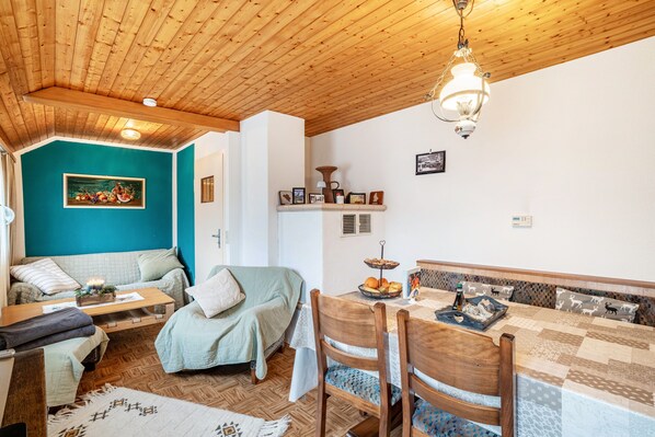 A cozy room with a wooden ceiling, a teal wall, a sofa, a dining table with chairs, and a hanging light fixture.