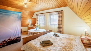 Une pièce chaleureuse avec un plafond en bois, un lit recouvert d’une courtepointe, une table de chevet avec une lampe et une fenêtre avec des rideaux.