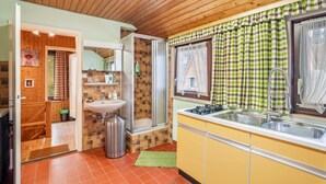 Une cuisine avec un évier, une fenêtre ornée de rideaux à carreaux et un plafond en bois.