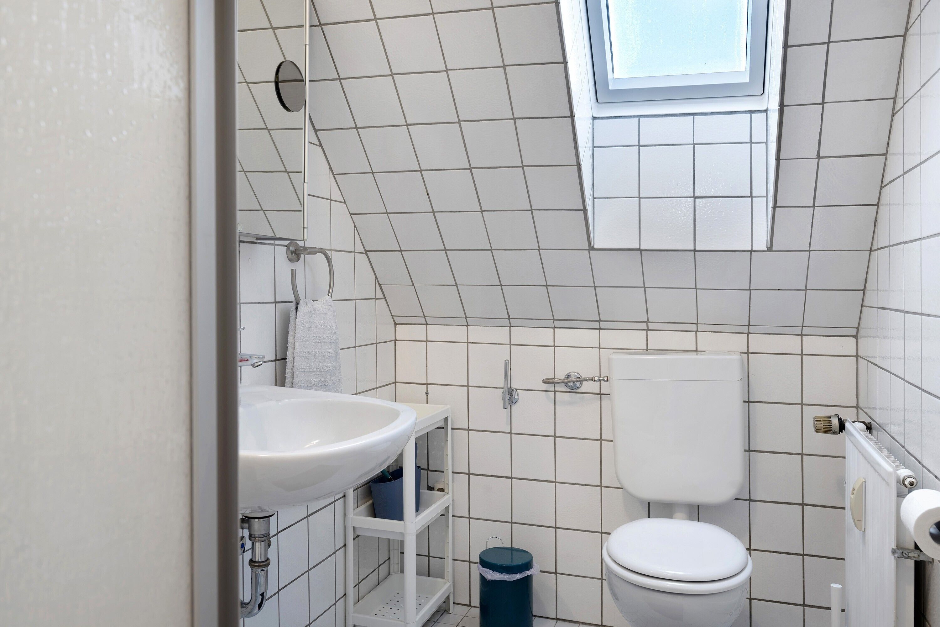 A bathroom with a white sink, toilet, and shower. There is a window above the shower.